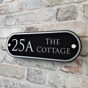 "Black and Silver House plaque that says ' on brickwork"The Cottage'
